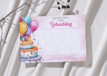 Personalisierbare Rubbelkarte zum Geburtstag mit gemalter Torte, Kerzen und bunten Luftballons. Die Karte liegt auf weichem, weißen Stoff neben einem trockenen Zweig. Auf der Vorderseite sind sechs leere Rubbelfelder und der Text „Rubbeln und gewinnen! Fi